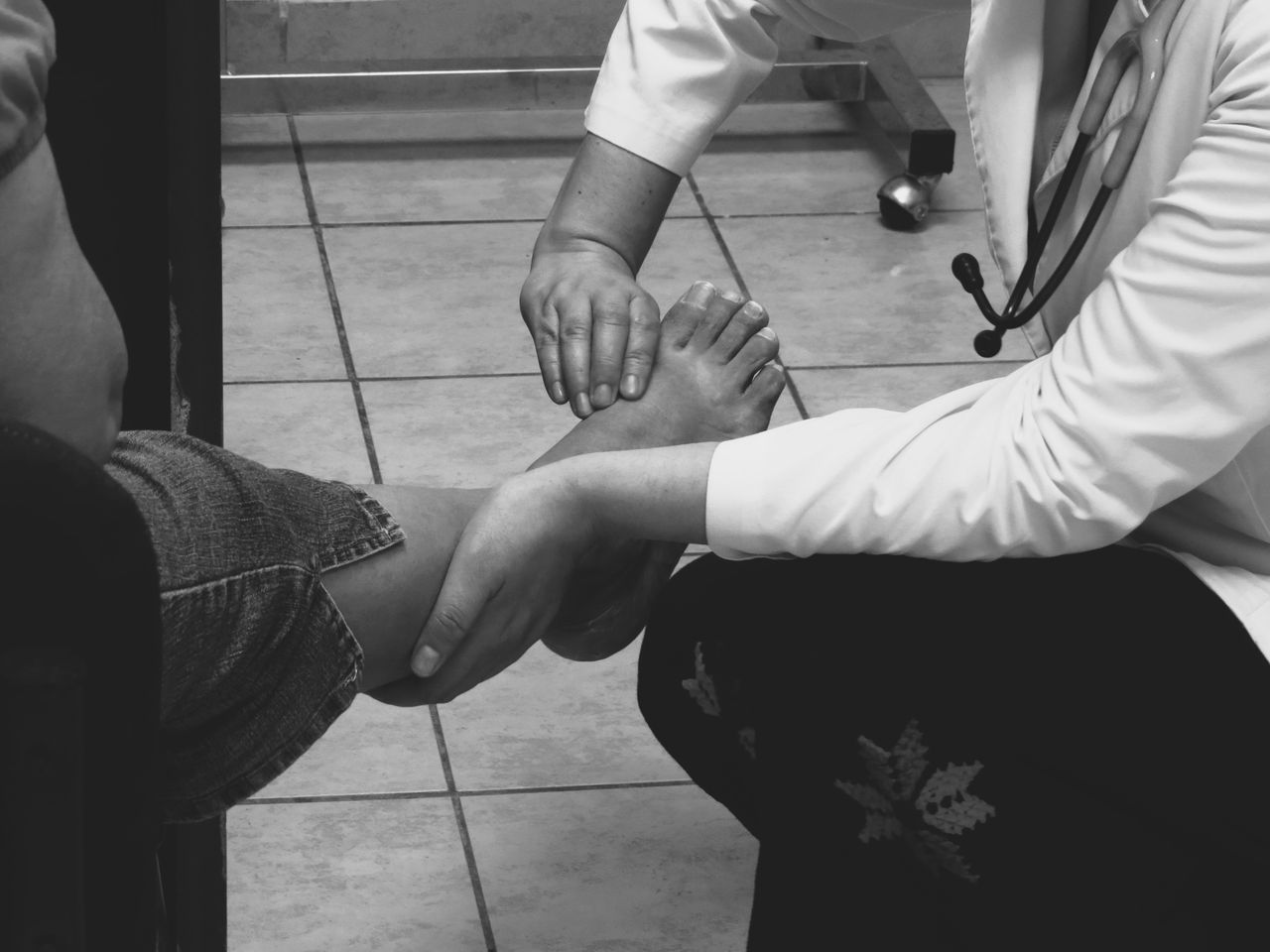Home Doctor examines a patient's foot during a medical consultation in a clinic setting.